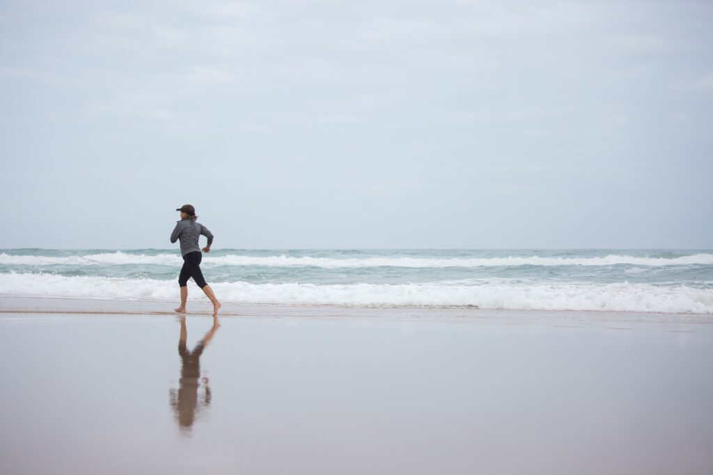 A woman runs on a serene beach, reflecting fitness and healthy lifestyle at sunrise.