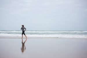 Advice & Resources A woman runs on a serene beach, reflecting fitness and healthy lifestyle at sunrise.