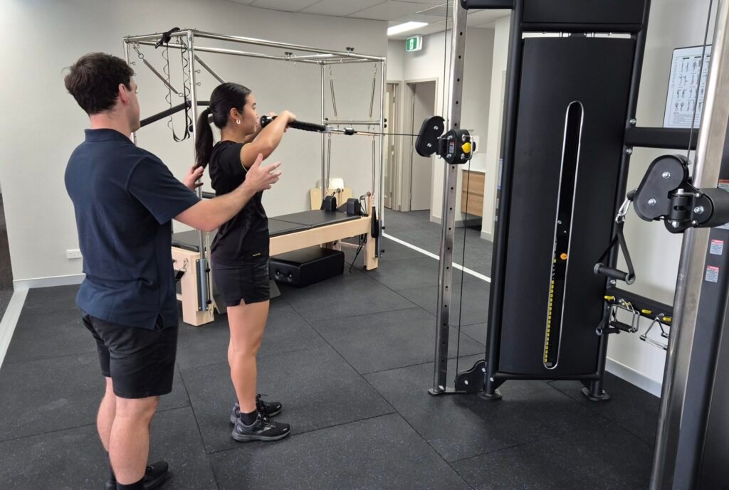 Physio teaching an exercise using a Functional Trainer machine in the gym